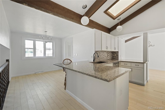 kitchen featuring a sink, stone countertops, a peninsula, and light wood finished floors