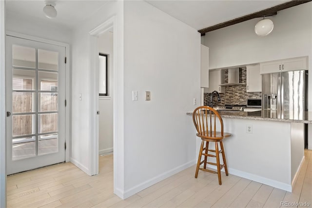 kitchen with a breakfast bar, light wood-type flooring, stainless steel microwave, wall chimney range hood, and decorative backsplash