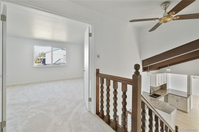 corridor with baseboards, an upstairs landing, a sink, and light colored carpet
