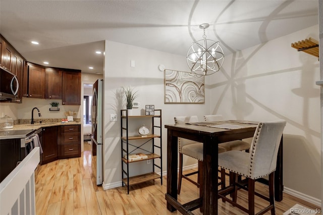 kitchen featuring stainless steel microwave, dark brown cabinets, light wood-style flooring, an inviting chandelier, and a sink