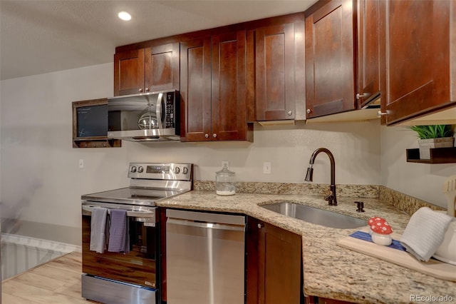 kitchen with a sink, light stone counters, wood finished floors, recessed lighting, and appliances with stainless steel finishes