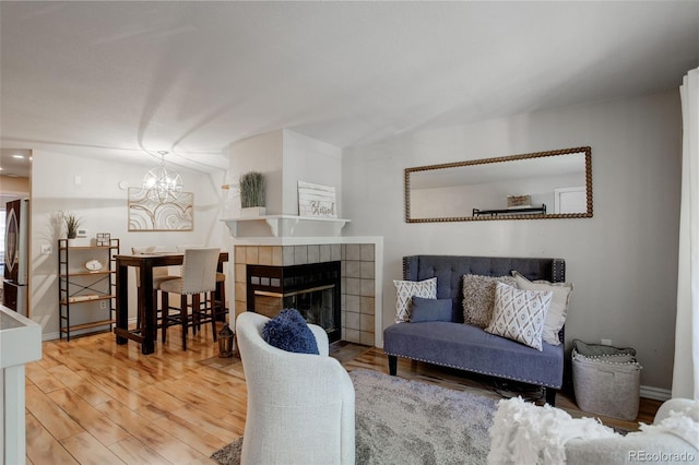 living room with a chandelier, baseboards, wood finished floors, and a tiled fireplace