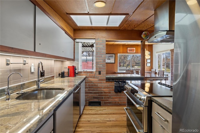 1400 E Bates Ave, Englewood, CO 80113 - kitchen featuring stainless steel appliances, a sink, wall chimney exhaust hood, light wood finished floors, and light stone countertops