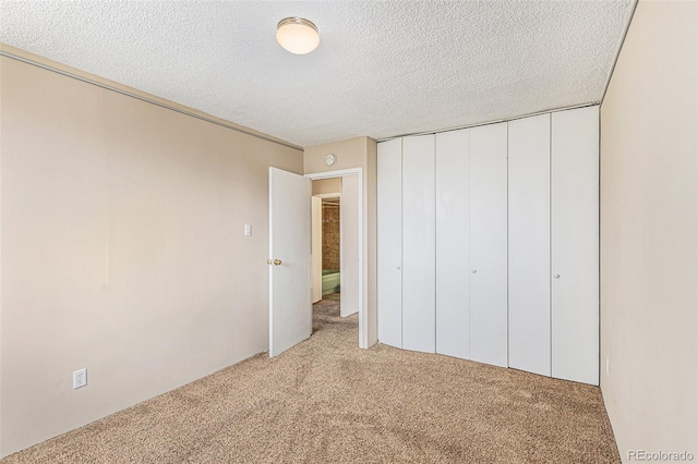 unfurnished bedroom featuring a textured ceiling, a closet, and light colored carpet