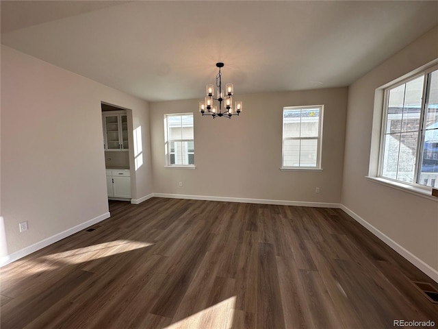 unfurnished room with plenty of natural light, an inviting chandelier, and dark hardwood / wood-style flooring