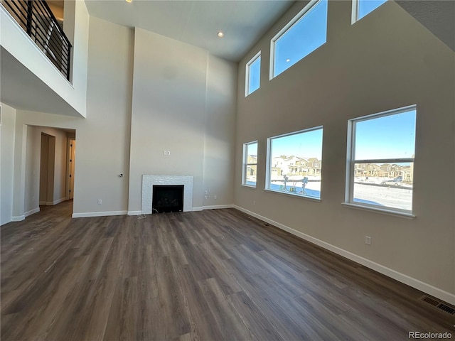 unfurnished living room featuring a high ceiling, a tile fireplace, and dark hardwood / wood-style flooring