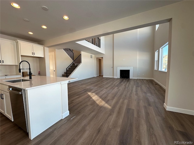 kitchen with stainless steel dishwasher, sink, dark wood-type flooring, white cabinets, and a center island with sink