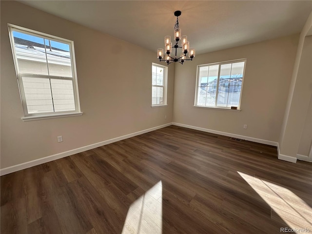 empty room featuring plenty of natural light, dark hardwood / wood-style floors, and an inviting chandelier