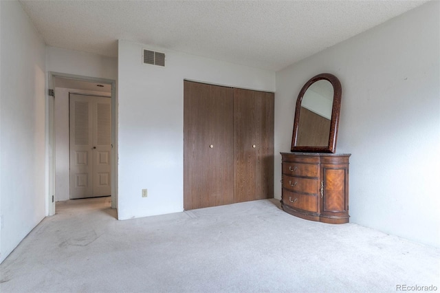 unfurnished bedroom with light carpet, a closet, and a textured ceiling