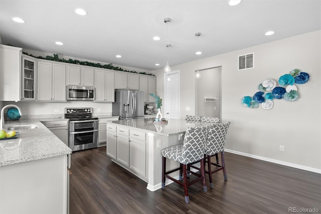 kitchen featuring visible vents, a sink, dark wood-style floors, appliances with stainless steel finishes, and a breakfast bar area