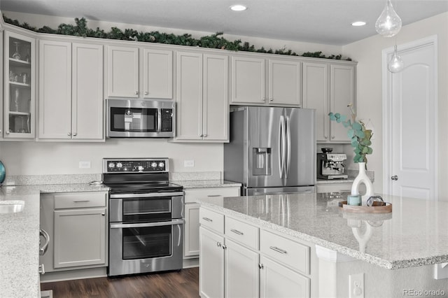 kitchen featuring light stone counters, decorative light fixtures, dark wood finished floors, appliances with stainless steel finishes, and glass insert cabinets