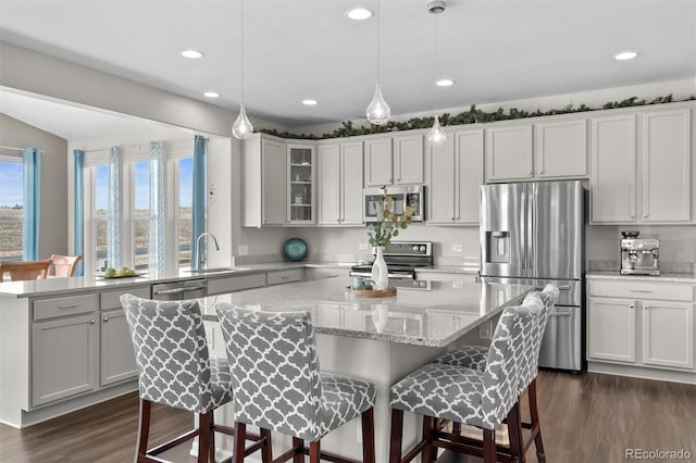 kitchen featuring a kitchen island, dark wood-type flooring, a breakfast bar area, appliances with stainless steel finishes, and a sink