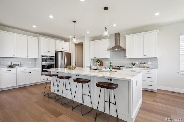 14337 Shasta Daisy Pt, Parker, CO 80134 - kitchen with wall chimney exhaust hood, appliances with stainless steel finishes, light wood-type flooring, decorative backsplash, and a kitchen bar