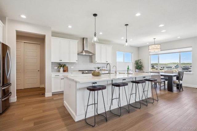 14337 Shasta Daisy Pt, Parker, CO 80134 - kitchen featuring wall chimney range hood, freestanding refrigerator, light wood-type flooring, a kitchen bar, and recessed lighting