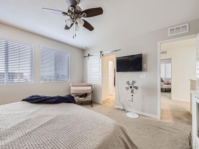 carpeted bedroom with ceiling fan, a barn door, and a textured ceiling