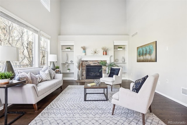 living room featuring dark wood-type flooring, a fireplace, built in features, and a high ceiling