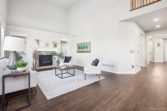 living room with a stone fireplace, a towering ceiling, built in features, and dark hardwood / wood-style floors