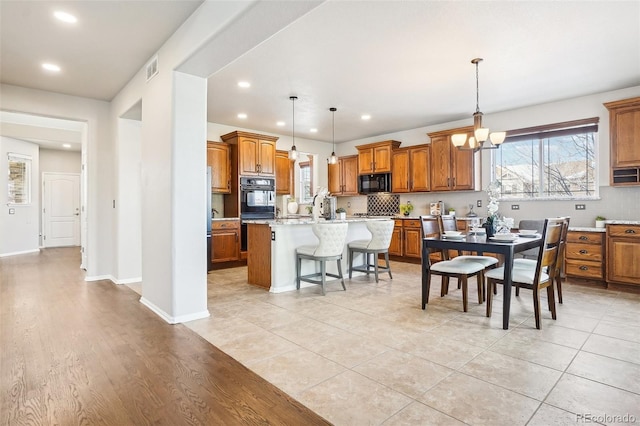 kitchen with a breakfast bar, pendant lighting, a kitchen island with sink, black appliances, and light stone countertops