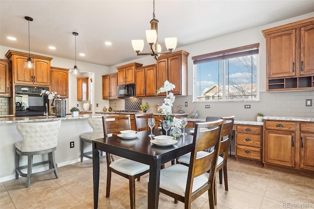 kitchen with decorative light fixtures, backsplash, a kitchen bar, black appliances, and light stone countertops