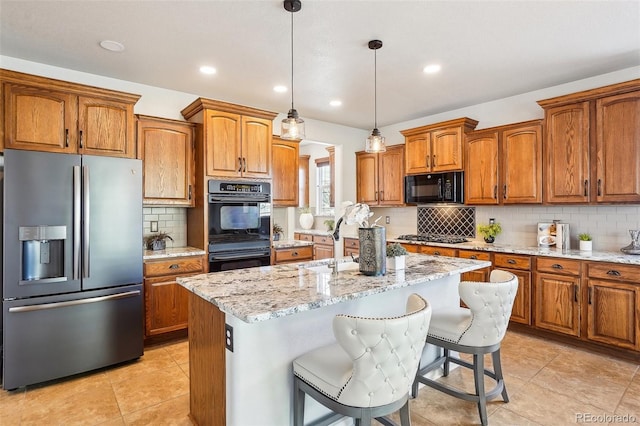 kitchen with a kitchen island with sink, sink, light stone counters, and black appliances