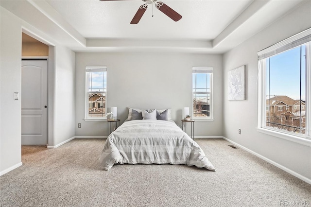 bedroom featuring multiple windows, a raised ceiling, and ceiling fan