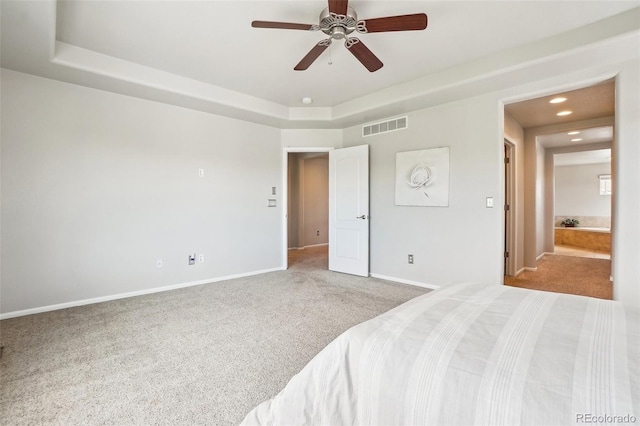 bedroom with light carpet, ensuite bath, a tray ceiling, and ceiling fan