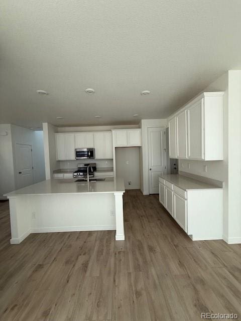 kitchen featuring wood finished floors, appliances with stainless steel finishes, white cabinetry, and a sink