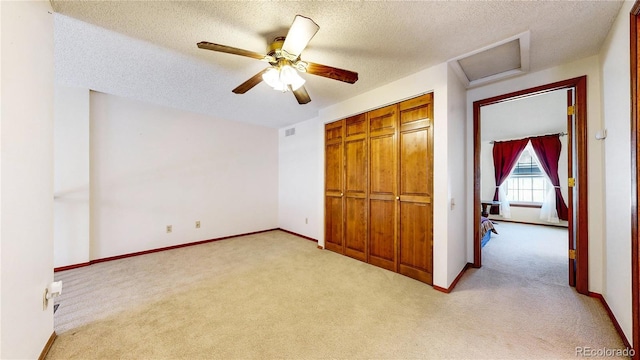 unfurnished bedroom with light carpet, a closet, attic access, and baseboards