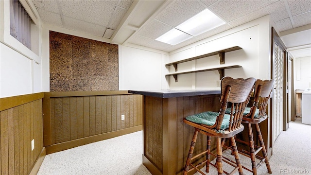 bar with washer / dryer, a paneled ceiling, light carpet, and a bar