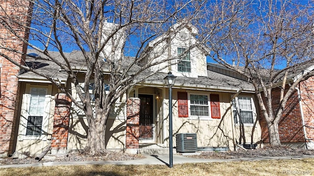 view of front of house featuring a shingled roof, central AC unit, and brick siding