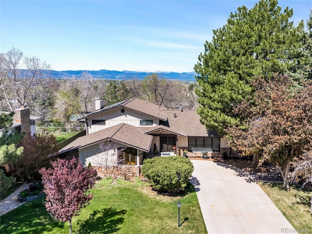 view of front of house featuring concrete driveway, a chimney, a mountain view, and a front yard