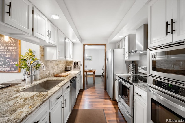 kitchen with wall chimney range hood, stainless steel appliances, a sink, and white cabinetry