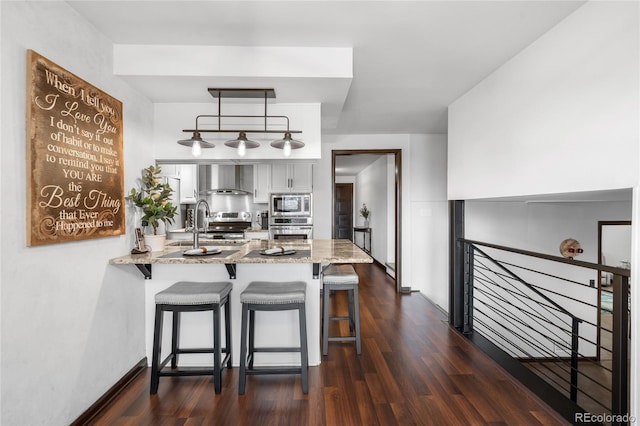 kitchen featuring wall chimney range hood, white cabinets, a peninsula, stainless steel appliances, and dark wood-type flooring