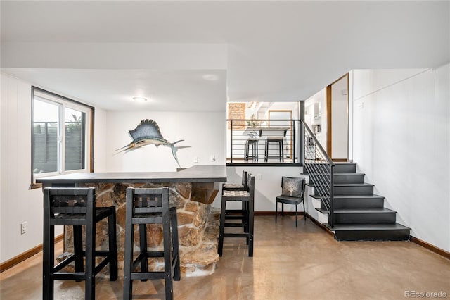bar featuring baseboards, bar, stairway, and finished concrete flooring