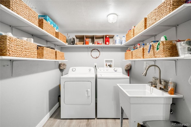 washroom with laundry area, washing machine and clothes dryer, a sink, baseboards, and light wood finished floors