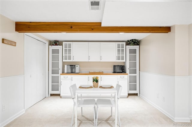 kitchen with black microwave, beam ceiling, white cabinets, white microwave, and glass insert cabinets
