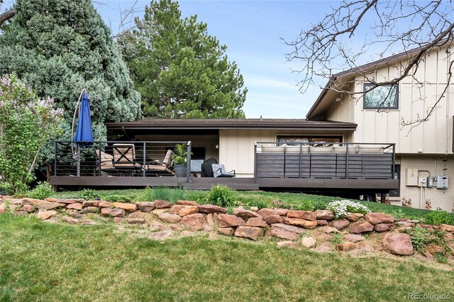 rear view of house with board and batten siding, a lawn, and a wooden deck