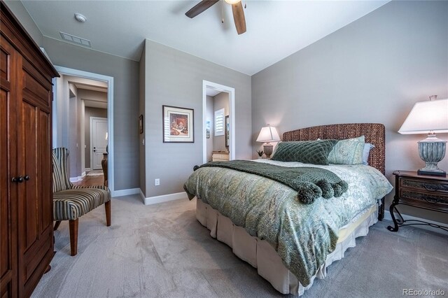 bedroom with ceiling fan, light carpet, baseboards, ensuite bathroom, and visible vents