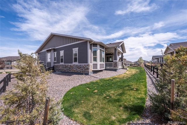 view of side of property with board and batten siding, covered porch, a lawn, fence, and stone siding