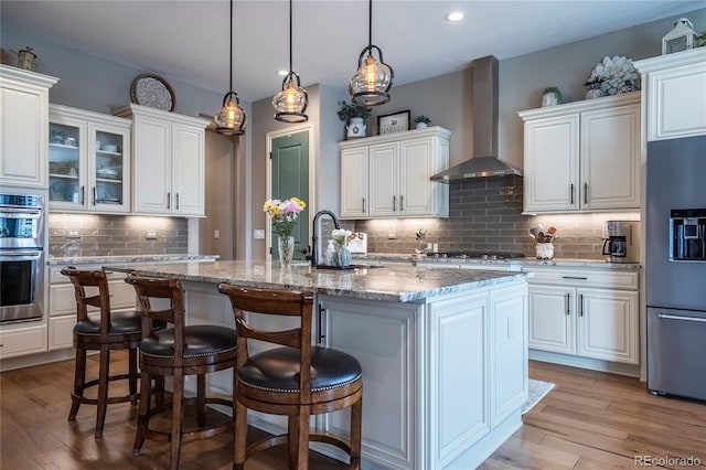 kitchen with fridge with ice dispenser, white cabinets, double oven, and wall chimney exhaust hood