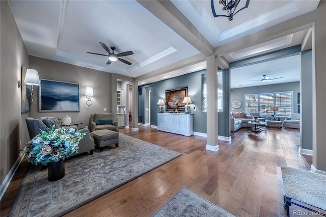 living room with baseboards, ceiling fan, wood finished floors, and a tray ceiling