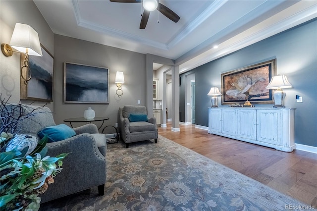 living area with crown molding, ceiling fan, baseboards, wood finished floors, and a tray ceiling