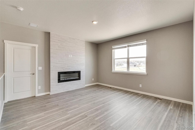 unfurnished living room with light hardwood / wood-style flooring, a large fireplace, and a textured ceiling