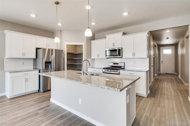 kitchen with sink, hanging light fixtures, stainless steel appliances, an island with sink, and white cabinets