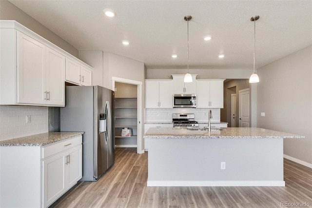 kitchen featuring decorative light fixtures, white cabinetry, sink, stainless steel appliances, and a center island with sink