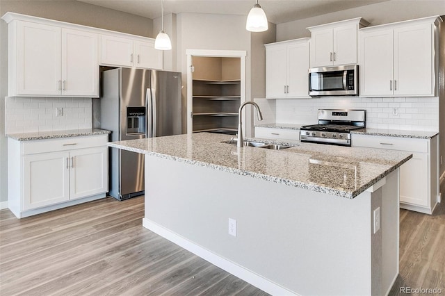 kitchen with a center island with sink, light wood-type flooring, hanging light fixtures, appliances with stainless steel finishes, and white cabinets