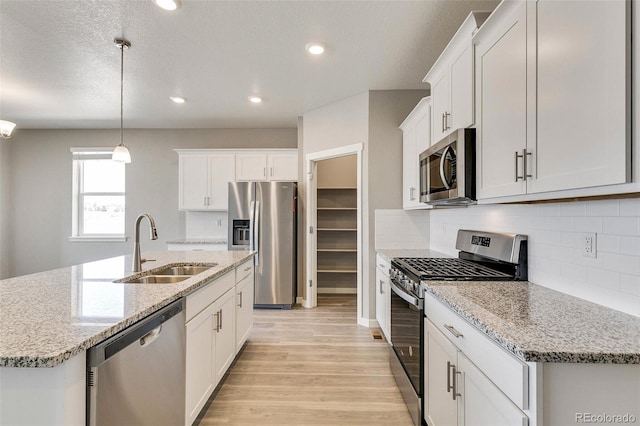 kitchen featuring sink, decorative light fixtures, appliances with stainless steel finishes, an island with sink, and white cabinets