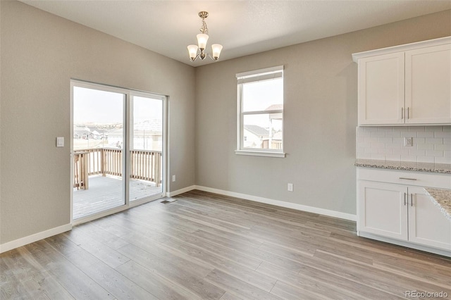 unfurnished dining area featuring plenty of natural light, a notable chandelier, and light hardwood / wood-style flooring