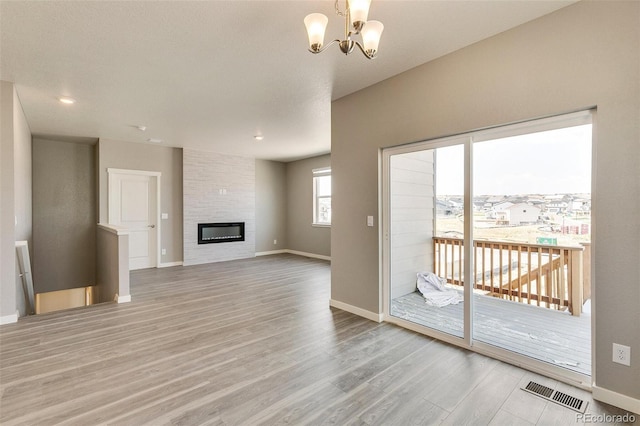 unfurnished living room with a notable chandelier, a fireplace, and light wood-type flooring