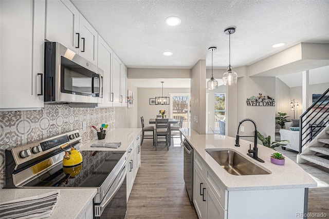 kitchen featuring appliances with stainless steel finishes, a sink, dark wood-style flooring, a center island with sink, and a textured ceiling